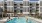 People enjoying the resort-style swimming pool at The Shipwright in Lynn, MA with sundeck chairs, shaded seating, and modern apartments